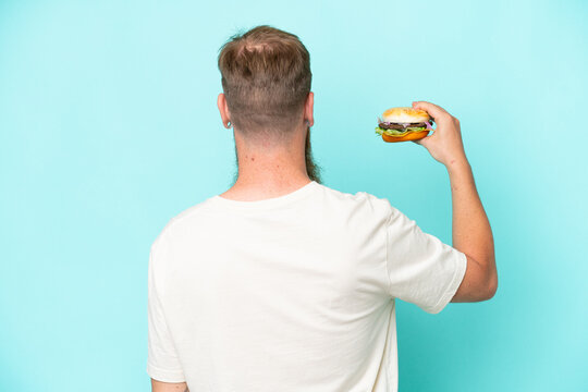 Redhead Man With Long Beard Holding A Burger Isolated On Blue Background In Back Position