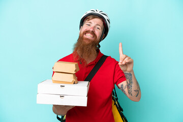 Delivery man holding pizzas and burgers isolated on blue background showing and lifting a finger in sign of the best