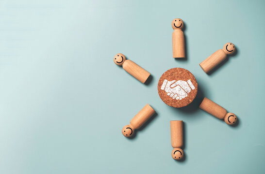 Top view design on blue background of Hand shaking which print screen on wooden round block with human figure for business deal and agreement concept.