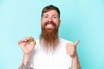 Redhead man with long beard holding a Bitcoin isolated on blue background pointing to the side to present a product