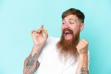 Redhead man with long beard holding a Bitcoin isolated on blue background celebrating a victory