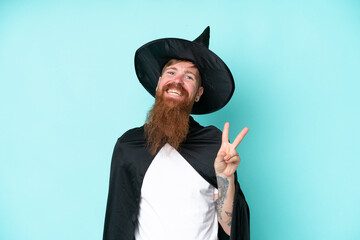 Young wizard in halloween isolated on blue background smiling and showing victory sign