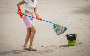 A female ecologist volunteer cleans the beach on the seashore from plastic and other waste