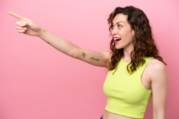 Young caucasian woman isolated on pink background pointing away