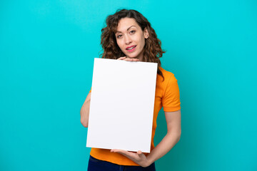 Young caucasian woman isolated on blue background holding an empty placard with happy expression