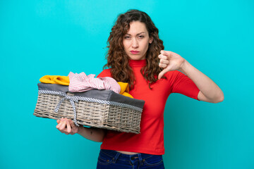 Young caucasian woman holding a clothes basket isolated on blue background showing thumb down with negative expression