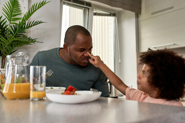 Boy touch nose of his father during having lunch