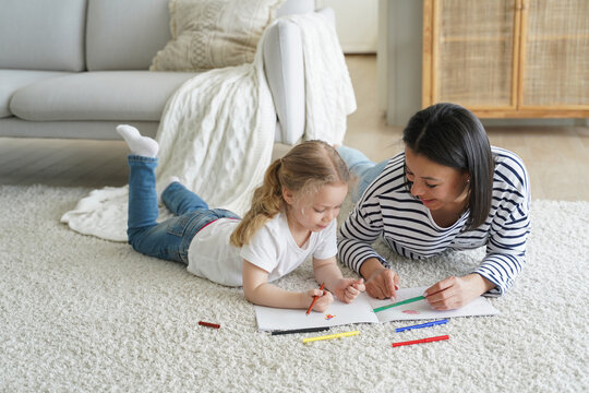 Kid girl daughter and mom drawing painting lying on floor carpet together. Children's education