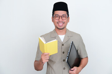 Indonesian teacher smiling at camera while holding a book and laptop