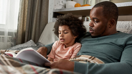 Adult father and little son reading book on sofa