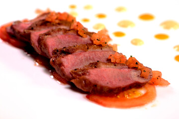 Fried pieces of a meat with sauce on a white plate. Grilled beef steak sliced on a white plate. Medium rare. Side view. .