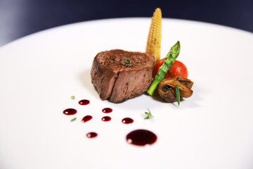 Tender grilled piece of meat with sauce on a white plate with isolated background. Fillet minion with corn, asparagus and tomato. Side view. Grilled steak sliced on a white plate.