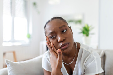 Portrait of unhappy African-American woman suffering from toothache at home. Healthcare, dental...