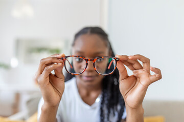 young African woman holds glasses with diopter lenses and looks through them, the problem of myopia, vision correction