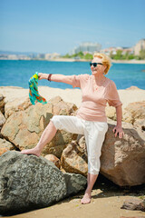 Happy mature woman smiling and having fun at beach. Summer portrait of senior woman walking on beach with a blue scarf