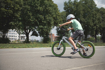 Obraz premium A school-age boy learns extreme tricks and extreme cycling in the city. Sporty child in protective gear riding a bicycle, cycling on the asphalt road outdoors. Sport. Active, healthy lifestyle concept