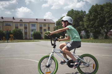 Obraz premium Side full-length of a sporty child boy in protective sports helmet, riding a bicycle in the city asphalt road. Active elementary age kid learning extreme cycling and tricks on his bike. Equilibre