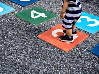 A little young boy standing on number 2 on multicolored hopscotch on the asphalt ground in the kids...