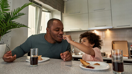 Boy feed pizza slice to dad during have breakfast