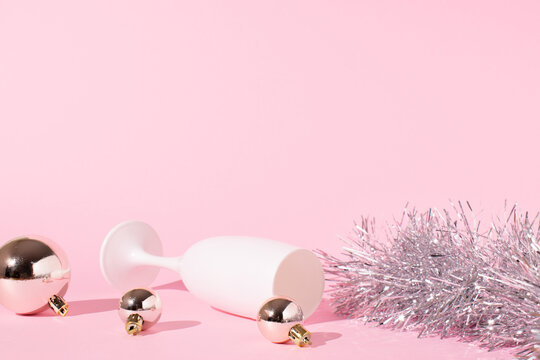 Champagne glass with boubles and shiny decorations. Pink background. New Year eve celebration concept.  Christmas party composition.