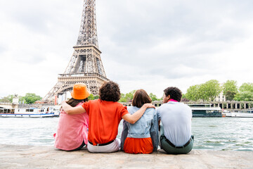Multiethnic group of young happy teens friends bonding and having fun while visiting Eiffel Tower...
