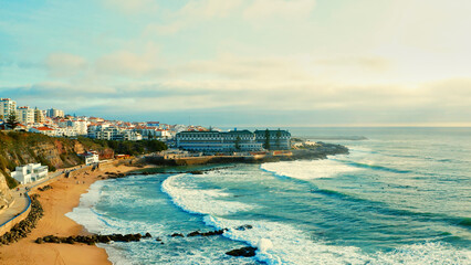 Drone view over sandy beach  touristic city Ericeira , Portugal. Aerial view - touristic coastline on summer while sunset. Beautiful seashore with skyline, waves and blue sky.