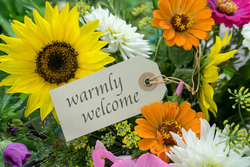 Colorful bouquet of summer flowers with card and english text:  warmly welcome