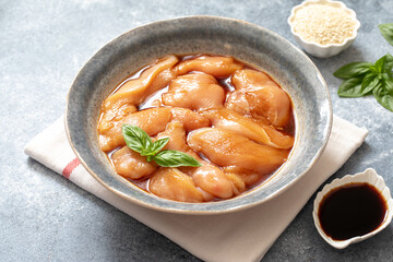 Raw diet marinated chicken meat with teriyaki sauce in a grey bowl. Marinating meat for cooking barbecue