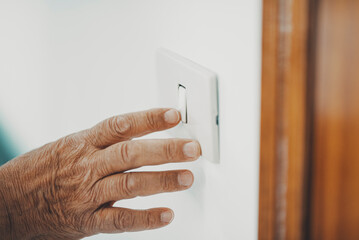 Close up of old hand senior woman switching off or on home light. Concept of saving bills for...