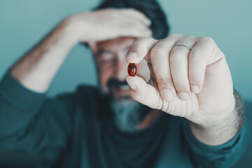 Close up of man holding red pill against migraine headache. Person in background holding and...