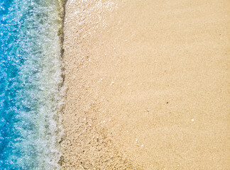 Beautiful beach background with clear and foamy blue sea water waves and clean white sandy beach. 