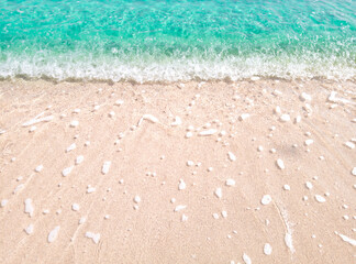 Beautiful beach background with clear and foamy blue sea water waves and clean white sandy beach. 