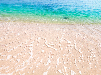 Beautiful beach background with clear and foamy blue sea water waves and clean white sandy beach. 