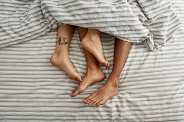 Cropped of barefoot couple under blanket on bed
