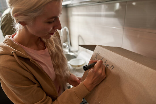 Girl writing 'kitchen' word on cardboard box