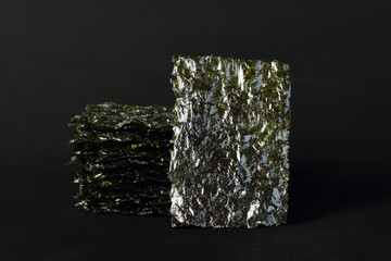 Seasoned seaweed snack. Algae sheets stacked in a pile on black  background. © Owl_photographer