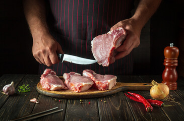 The hands of a cook or a butcher with a knife in the kitchen cut raw meat ribs. Cooking a delicious grill for a restaurant or hotel.