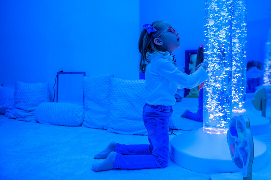 Child in sensory room, snoezelen, interacting with colored lights bubble tube lamp during therapy session. Child with cerebral palsy in occupational therapy.