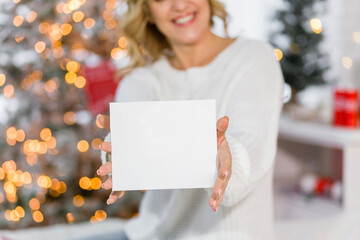 A beautiful brunette girl in a white sweater sits on a bed against the background of Christmas...