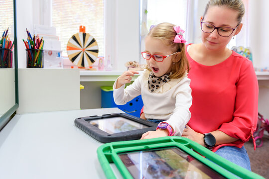 Non-verbal girl living with cerebral palsy, learning to use digital tablet device to communicate. People who have difficulty developing language or using speech use speech-generating devices.