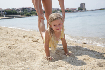 Mother and daughter playing on beach, exercising for a wheelbarrow race.	