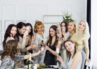 Girls pouring champagne into glasses. Ten adult female friends in sparkly evening dresses pose with glasses of champagne and celebrate the new year.