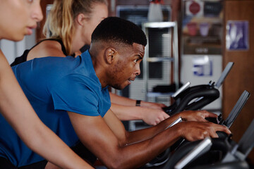 Fototapeta na wymiar Group of focused young multiracial adults doing cardio on exercise bike at the gym