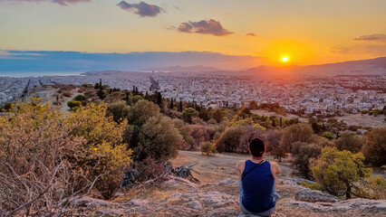 Tourist man watching the sunset over city of Athens seen from Filopappou Hill (hill of muses),...