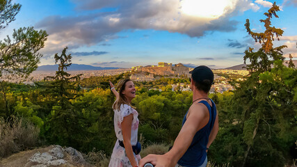 A young couple taking a selfie during sunset with panoramic view looking at Parthenon of the...