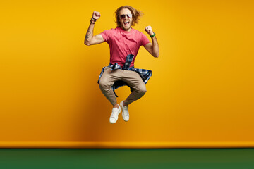 Fototapeta na wymiar Excited young man gesturing while jumping against yellow background