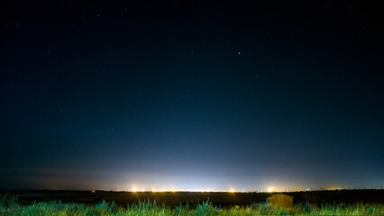 Glowing lights on the horizon at night under the starry sky and green grass