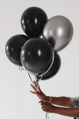 Woman hands holding black and silver balloons on white background.