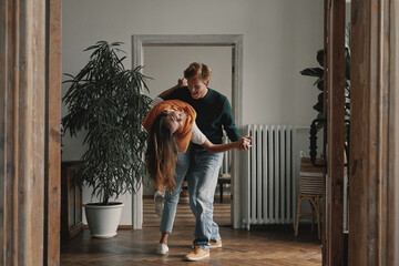 Full length of cheerful young couple dancing at home together