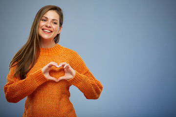 Smiling woman in warm orange sweater making heart with finger.